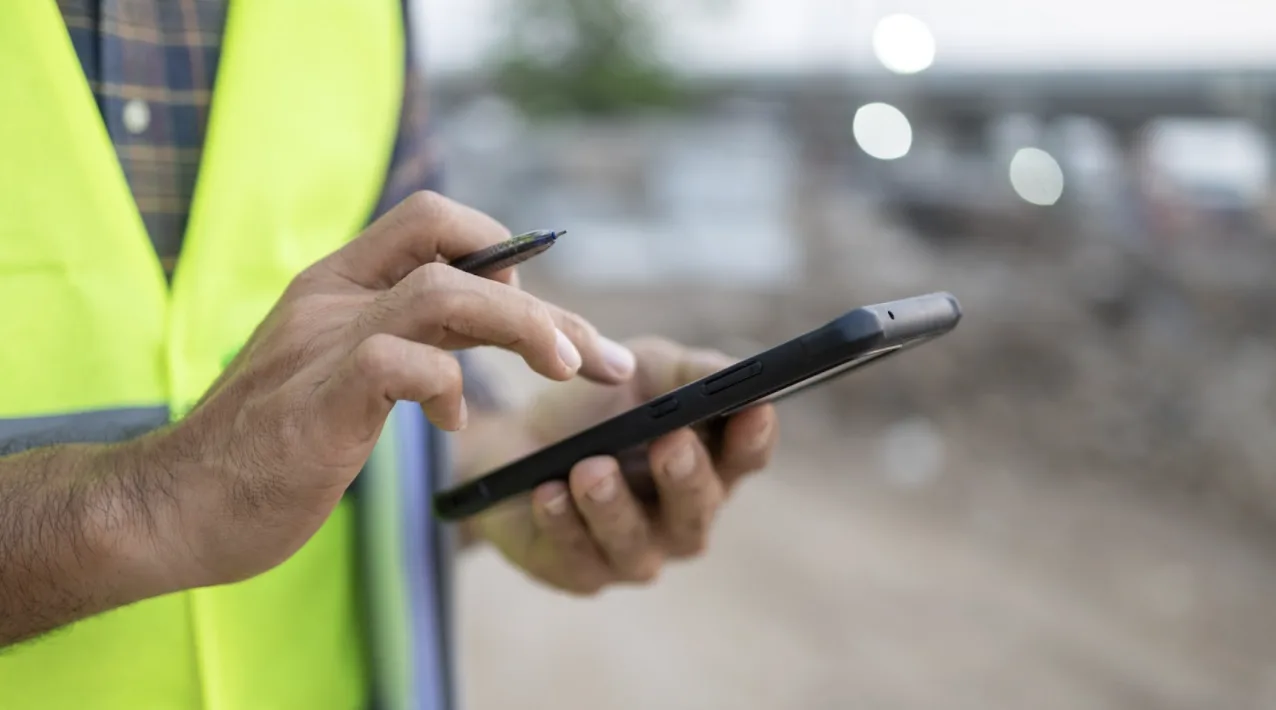 Uomo in cantiere scrive su uno smartphone